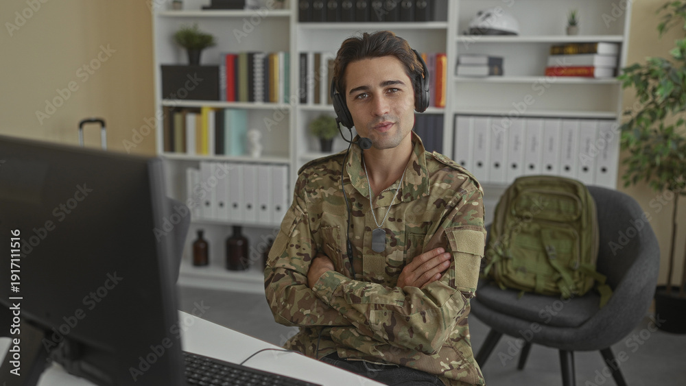 Fototapeta premium Soldier man typing with headset, hands on keyboard and dog tags visible while using a desktop computer at a desk with bookshelves and a backpack in an office building; duty.