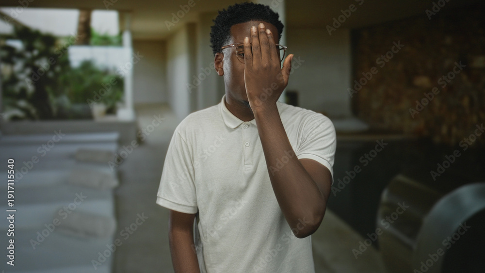 Fototapeta premium Man wearing glasses and polo shirt rubbing face with hand in indoor spa pool area with lounge chairs; fatigue.