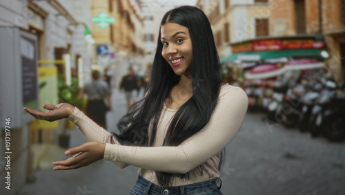 Photos Young latin woman presents open palms to camera with a gentle smile on sunlit city street; invitation