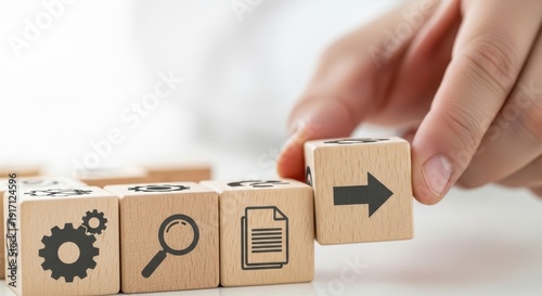 Wooden cubes featuring workflow diagram icons being set by hand using macro sharpness and soft white blur behind.