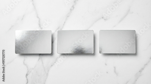 Set of three blank rectangular holiday gift cards in silver foil arranged on white marble surface with even studio lighting highlighting metallic sheen.
