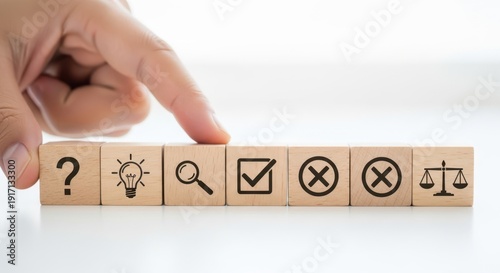 Decision making icons on wooden cubes being aligned by hand using cinematic shallow focus and white background blur effect.