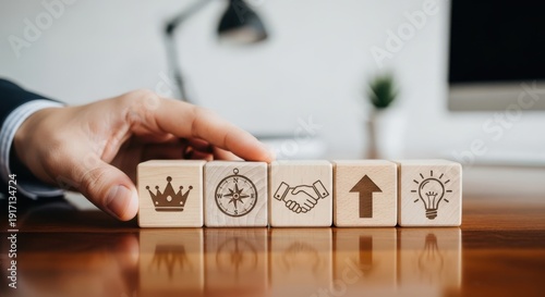 Hand aligning wooden cubes with leadership symbols using shallow focus and tastefully blurred minimal office background.