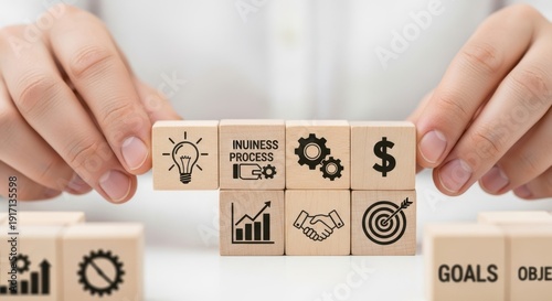 Hand arranging wooden cubes with business strategy icons using shallow depth of field and softly blurred white background.