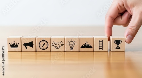 Leadership icons on wooden cubes aligned precisely by hand with shallow focus and clean minimal blurred desk backdrop.
