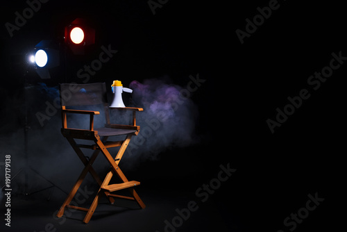 фотографія Film director's chair, megaphone and lighting equipment on black background with