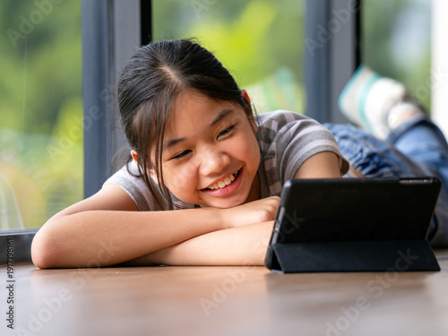 Wallpaper Mural Smiling young girl lying on wooden floor using tablet near window at home, online learning, digital education, child lifestyle, homeschooling, technology for kids concept Torontodigital.ca