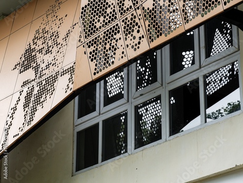 Modern building facade featuring orange perforated metal panels with circular patterns. Contemporary architectural design showing decorative cladding above windows in an urban setting.