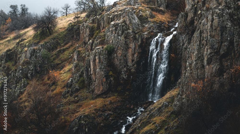 Obraz premium Cascading Waterfall Down a Rugged Rocky Cliffside in a Natural Landscape