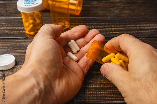 Obraz na plátně Hands hold pills while opening a bottle of medication on wooden table