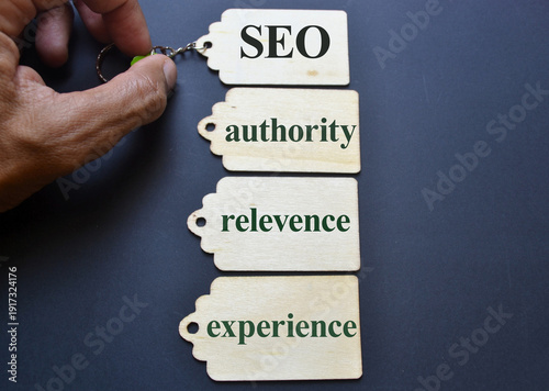 Hand holding keychain with wooden tags labeled seo authority relevance and experience on dark background symbolizing digital marketing strategy, search optimization, and online visibility for editoria