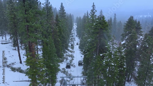 Drone aerial footage showing a chairlift line crossing a snow covered pine forest in Lake Tahoe, California, USA. Winter alpine scenery with fresh mountain snow.