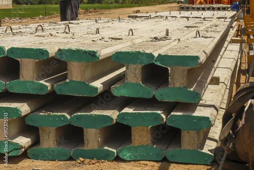 Precast concrete beams stacked at construction site, showcasing their green end caps and sturdy design for structural support. beams are ready for use in building projects