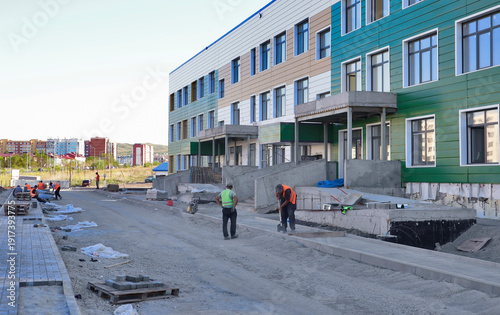 Final stage of new school construction in a modern residential district, with workers on site. Urban development project in progress, contemporary building. Ust-Kamenogorsk, Kazakhstan