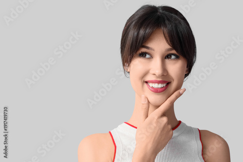 Thoughtful young woman with beautiful smile on light background, closeup