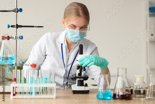 Female scientist with medical mask and microscope working in laboratory