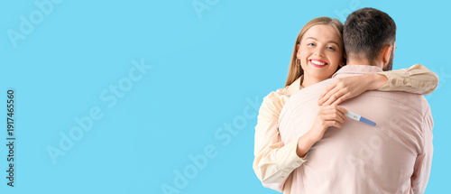 Happy young couple with pregnancy test hugging on blue background