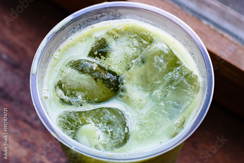 Close up of a Iced Matcha or Green Tea in Plastic Glass, High Angle View. Wooden table and place for text.

