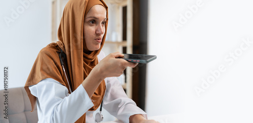 Canvas Print Muslim female doctor in hijab using smartphone for AI voice recognition in hospital or clinic