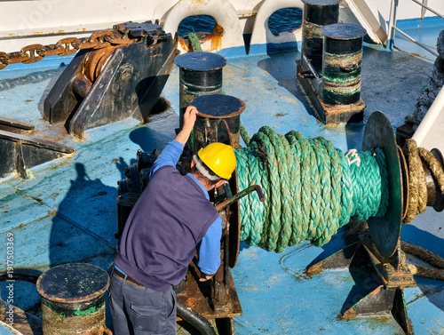 Canvas Print Worker with safety helmet operating winch with green rope on board a vessel