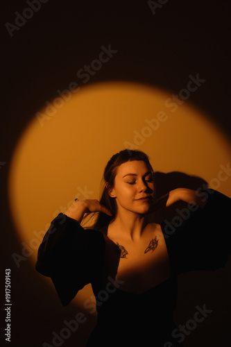 Moody warm portrait of woman in black dress with chest tattoos under circular spotlight for poster and editorial background design