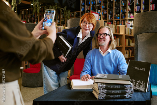 Bild auf Leinwand Caucasian middle aged man sitting at table signing book, Caucasian middle aged w
