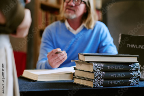 Foto Middle aged Caucasian man sitting at table signing books during presentation eve