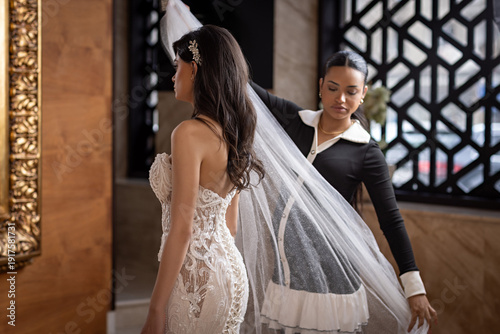 Bridal stylist adjusting veil on bride in lace gown