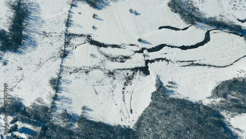 Aerial top view of winding river flowing through snow covered winter landscape