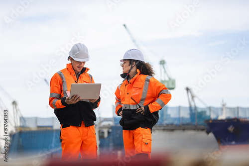 Billede på lærred Port industry engineers in safety uniforms using a laptop to manage logistics an