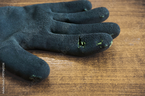 Black rubber working gloves with a hole on wood surface, space for text.