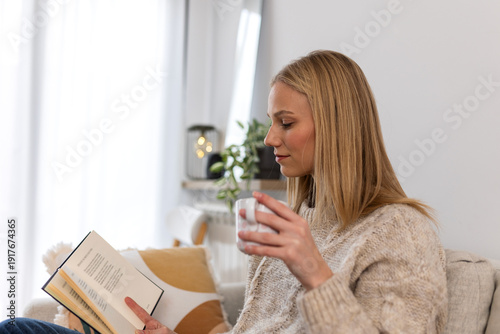 Fotografie Woman drinking coffee and reading book on sofa