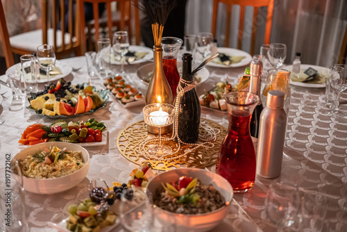 Photos Beautifully arranged dinner table with assorted appetizers, fruits, salads, wine bottles, and candles in warm ambient lighting