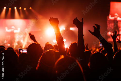Crowd with fists and hands raised cheering at red music concert