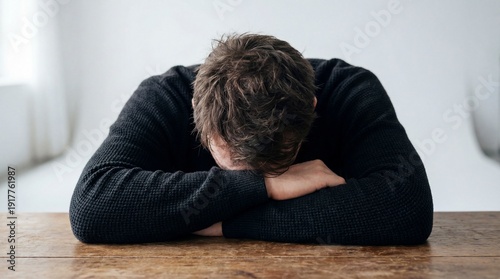 A man deeply burdened by his thoughts, with his head resting on the table, expressing a sense of heavy emotions. Capturing feelings of dejection and isolation.