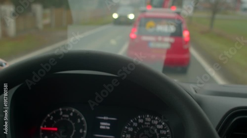 Suburban traffic with cautious driver proximity, Male driver closely following vehicle in quiet neighborhood traffic, White male driver maintaining safe gap behind red vehicle in suburban area