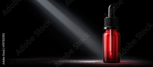 Red dropper bottle with light beam on black background.