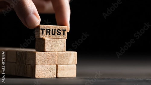 Building Trust Concept: Hand Placing Wooden Block with 'TRUST' Inscription on a Dark Backdrop