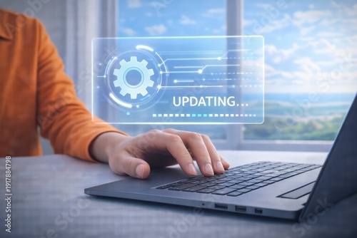 Person in orange shirt working on laptop with updating progress bar on screen by window with landscape view JPG image