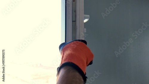 A worker wearing work gloves repairs a plastic window