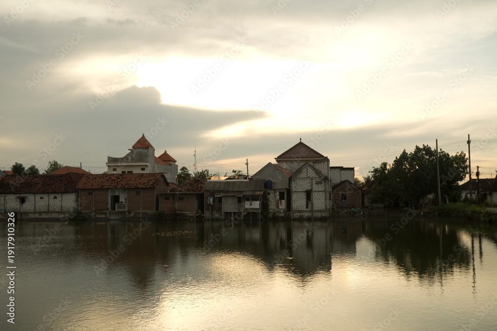Obraz premium Peaceful Evening Landscape with Water Pond Between Houses