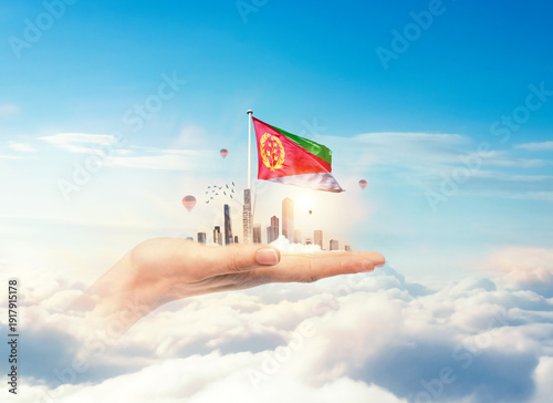 Photos Eritrea flag rising above a modern city held in a hand over clouds symbolizing growth, patriotism, and a bright future