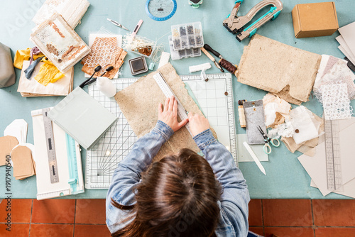 Woman Creates Scrapbook Using Paper, Tools, and Supplies on Table in Her Crafting Space