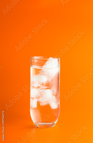 An iced cocktail in a HiBall Glass against an orange background.
