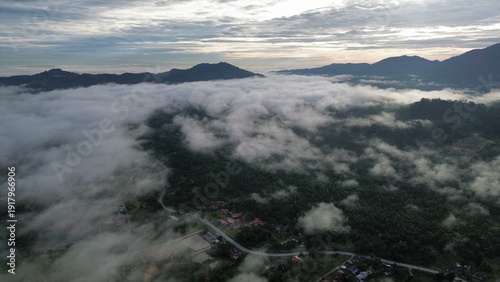 Foto Drone aerial view of misty clouds floating over green forest and rural village in a mountainous landscape during early morning