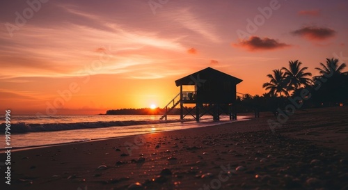 Beach hut silhouetted against a vibrant sunset sky; water glistens; palm trees in shadows