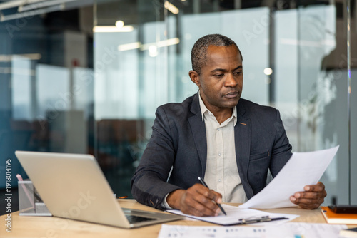 Photos Mature afro executive concentrating on legal documents at his desk, reviewing co