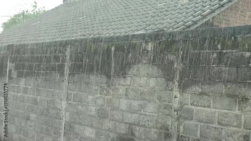 Heavy rain against a backdrop of walls and buildings in a rural setting.