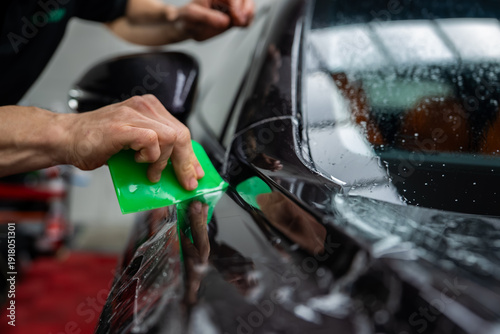 Tableau sur toile A technician uses a bright green squeegee to smooth clear film near a door seam and side mirror, with bead like water droplets and shallow depth of field emphasizing care