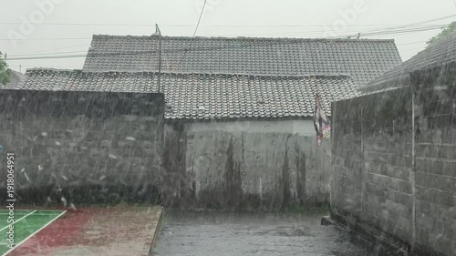 Heavy rain against a backdrop of walls and buildings in a rural setting.